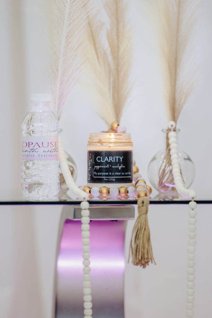 Clarity candle by Wicks by Grey lit on a glass table with beads and pampas grass, featured in the Menopause Rebirth Podcast Episode 1 as a symbol of understanding during menopause.