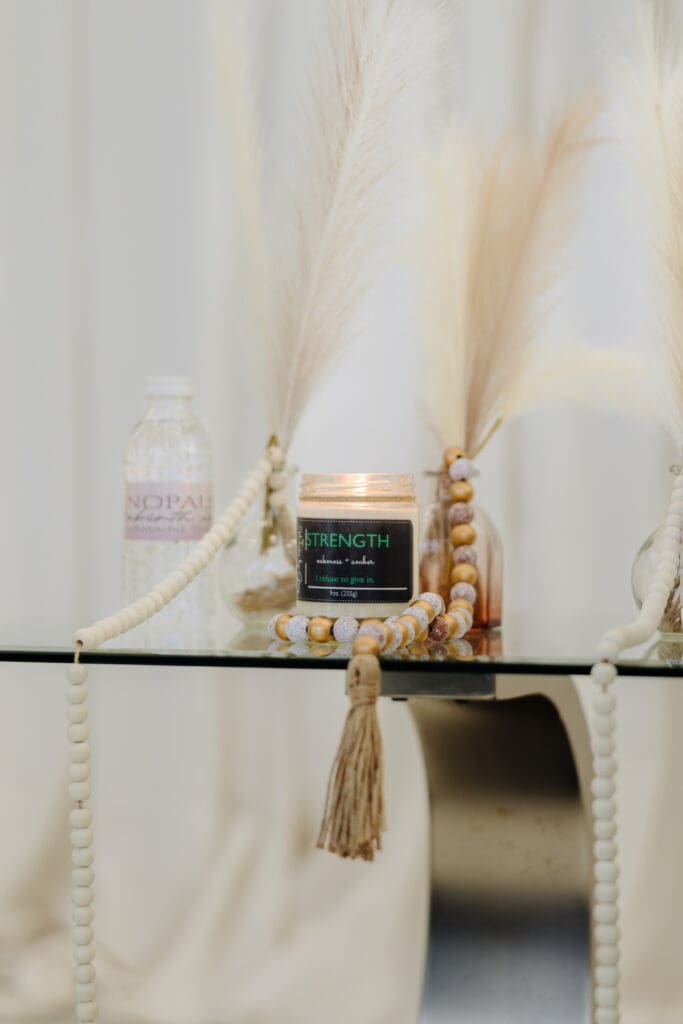 Strength candle by Wicks by Grey, lit on a glass table with beads and pampas grass, featured in the Menopause Rebirth Podcast Episode 2 to symbolise resilience during menopause.