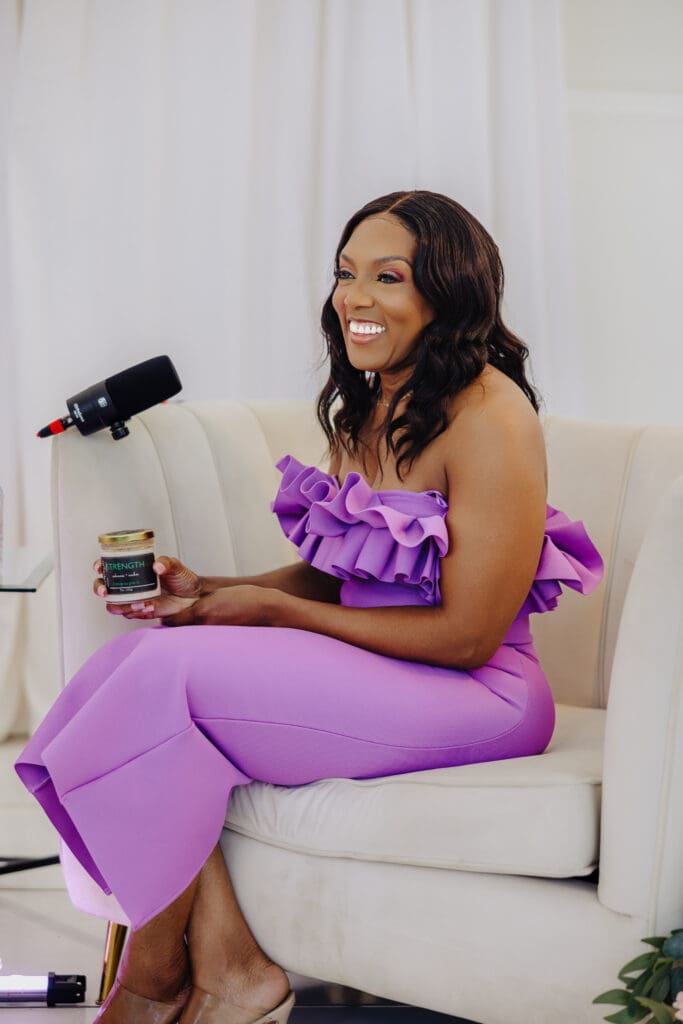 Dr Charmaine Thomas smiling while recording the Menopause Rebirth Podcast, holding the Strength candle by Wicks by Grey, symbolising resilience during menopause.